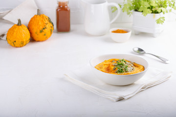 Spicy pumpkin soup served with pumpkin seeds and parsley.  Bowl with autumn squash soup on white table.