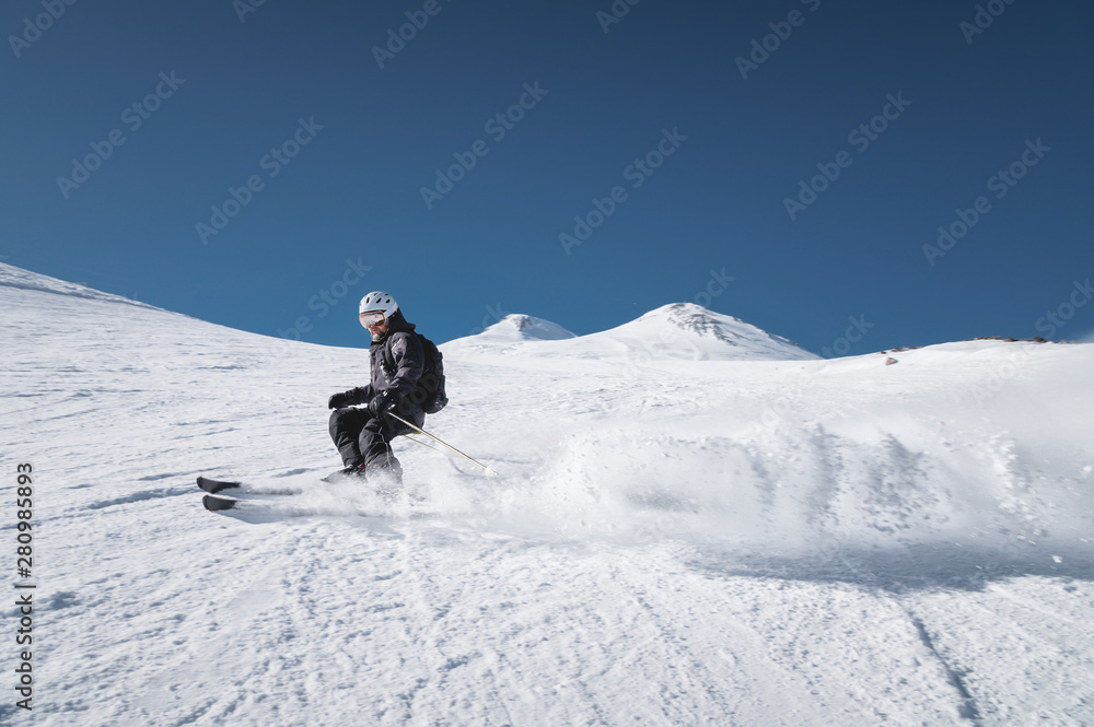 Wall mural a bearded mature aged male skier in a black ski suit descends along the snowy slope of a ski resort 