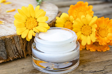 Obraz na płótnie Canvas A jar of white cosmetic cream for body care. Fresh orange calendula flowers on wooden background.