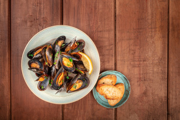 Marinara mussels, moules mariniere, shot from the top on a dark rustic wooden background with toasted bread and a place for text