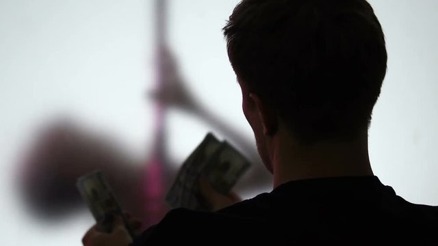 Young man watching striptease dance counting dollars in hands, night relax