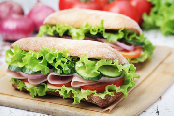 Two sandwiches with fresh vegetables, ham and cheese in ciabatta bread