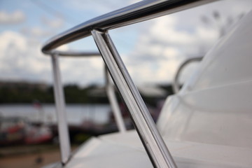 Stainless steel railing on white deck of a motor boat close-up on a blurred background of blue sky,...