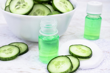 Sliced cucumber and a bottle of cucumber extract on a white wooden table and a white background. Liquid cosmetics for skin care.