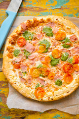 Pizza with parma ham, cheese, green pesto and tomatoes 