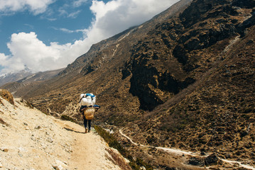 Porter and Sherpa walking with big bag baggage luggage in Himalaya Mountains in Nepal.