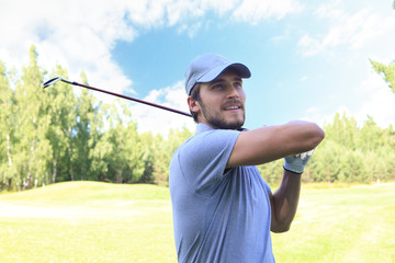 Golfer hitting golf shot with club on course while on summer vacation.