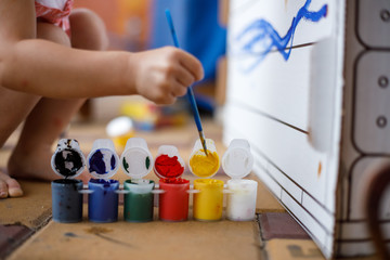 Girl paints a cardboard house at summer day, outdoor