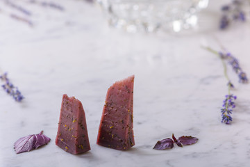 Two slices of lavender cheese, lavender flowers and basil leaves on white marble worktop