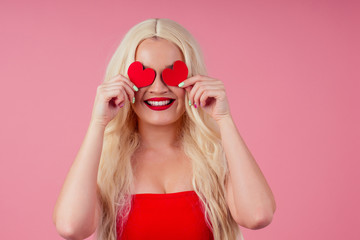 Closeup portrait of beautiful blond girl holding in hands paper heart isolated on pink background, Valentine day celebration