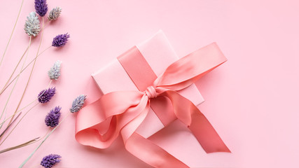 Pink gift box with a pink ribbon on a pink  background decorated with  dried flowers of gently purple color .  Holiday concept.  Flat lay.