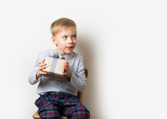 Scandinavian lifestyle minimalism christmas and new year concept with kid - little boy with stack of gift box on a chair in room, white background