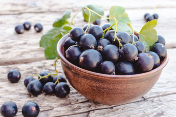 Fresh ripe currant berries in a bowl on wooden background near green leaves. Juicy fruits currants. Black currant