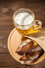 Oktoberfest holiday concept. Beer, smoked fish, chips on a wooden textural background in a dark key. Beer in a glass, fish in paper close-up and copy space.