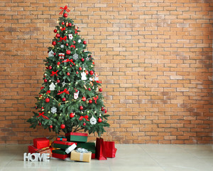 Beautifully decorated Christmas tree with gift boxes near brick wall