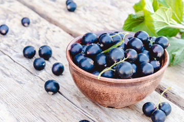 Fresh ripe currant berries in a bowl on wooden background near green leaves. Juicy fruits currants. Black currant
