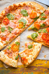Pizza with parma ham, cheese, green pesto and tomatoes 