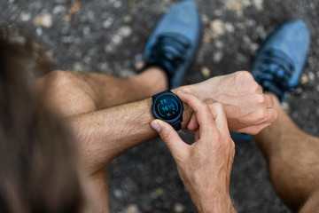 Fit man checking smart watch wearable technology sport smartwatch on fitness run walk outside. Top view from above with running shoes in street. © Maridav