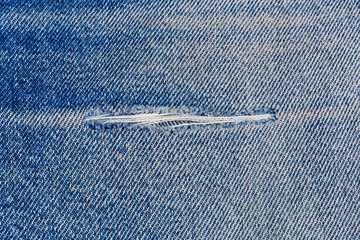 Hole on denim jeans with frayed threads close-up