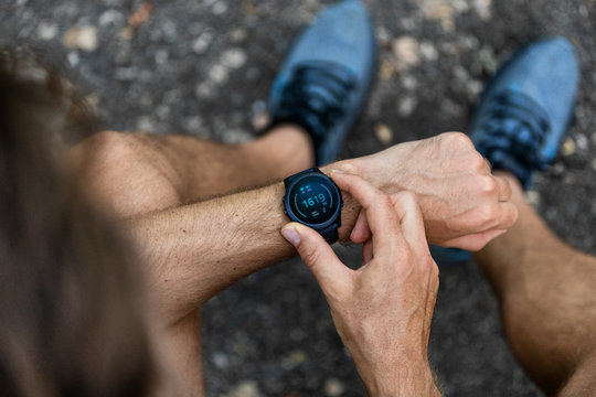 Fit man checking smart watch wearable technology sport smartwatch on fitness run walk outside. Top view from above with running shoes in street.
