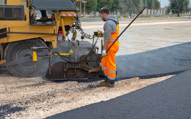 Worker regulate tracked paver laying asphalt heated to temperatures above 160 ° pavement on a runway
