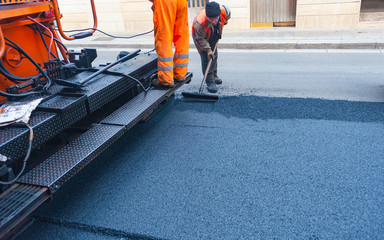 Worker regulate tracked paver laying asphalt heated to temperatures above 160 ° pavement on a runway