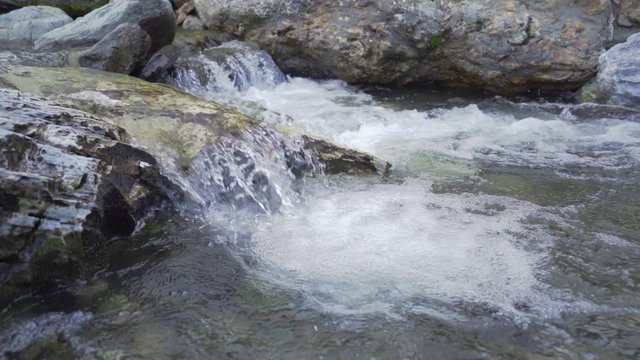 Close up of water stream with white and transparent bubbles. Slow motion.