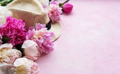 Pink peonies and hat on a pink concrete background
