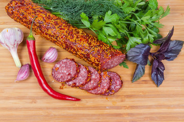 Top view partly sliced salami with mustard coating among greens