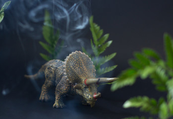 Realistic figure of the triceratops dinosaur under juicy green leaves on the smoky black background