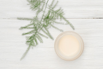 Facial cream in a jar on a white wooden table background.