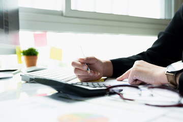Close up Business woman using calculator and laptop for do math finance on wooden desk in office and business working background, tax, accounting, statistics and analytic research concept