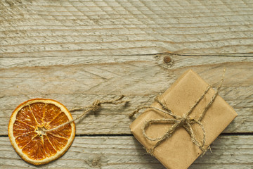 Christmas decor. Dried orange slice and gift box in craft paper on wooden background,  top view, minimal flat lay