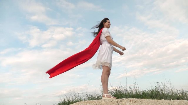 cheerful woman plays in a red cloak with expression of dreams. girl dreams of becoming a superhero. girl fooling around standing on a field in a red cloak, playing superhero.