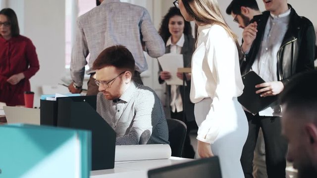 Stressed and tired young Caucasian businessman manager working at busy modern office, woman puts documents on his table.