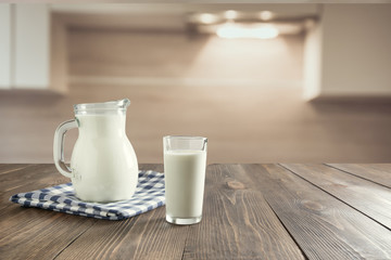 Fototapeta na wymiar Glass of fresh milk and jug on wooden tabletop with blur kitchen as background for montage product.