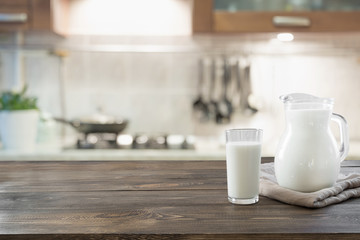 Glass of fresh milk and jug on wooden tabletop with blur kitchen as background for montage product.