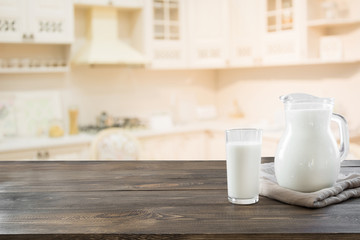 Glass of fresh milk and jug on wooden tabletop with blur kitchen as background for montage product.