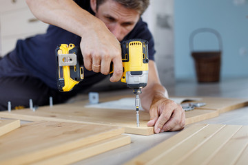 Man assembling furniture at home using a cordless screwdriver