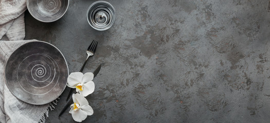 Elegance table setting with knitted grey napkin, cutlery, ceramic plates, glasses and white orchid flowers