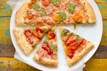 Pizza with parma ham, cheese, green pesto and tomatoes 
