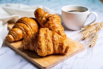 freshly baked croissants on wooden cutting board with coffee.