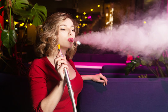Woman in the red clothes dress smokes a hookan at the hookah bar. The pleasure of smoking shisha