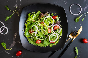 Eat green concept with organic fresh vegetable salad in ceramic plate on black background.