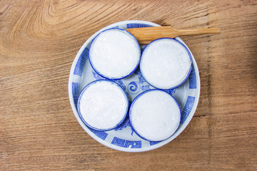 Thai Coconut Milk Custard is a thai dessert made from rice flour, coconut milk and sugar put the small ceramic cups place are on a wooden floor. Khanom Thuai,