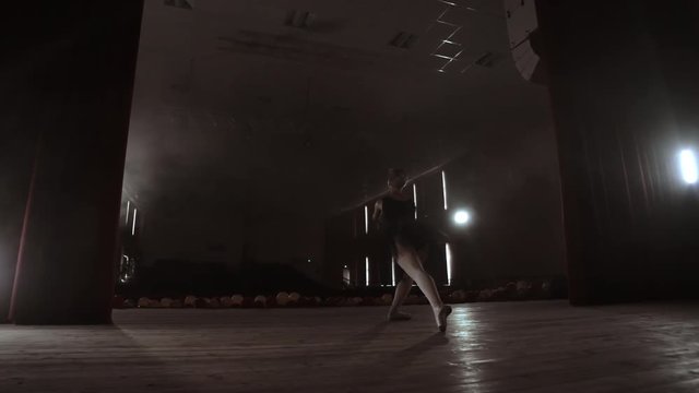 Slow motion: prima ballet in a black dress performs rotations and dance graceful movements rehearsing a solo program. The camera moves on gimbal