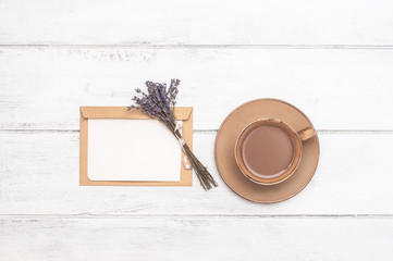 A cup of coffee with milk, an envelope and blank paper with a bouquet of lavender on a white wooden background. Postcard. Good morning. Gentle romantic atmosphere. Flat lay, Top view