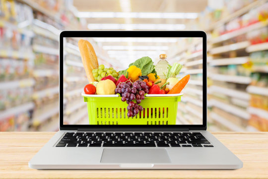 supermarket aisle blurred background with laptop computer and shopping basket on wood table grocery online concept