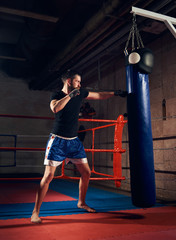 handsome male fighter training hard kickboxing and preparing for fight, kicking and punching heavy...