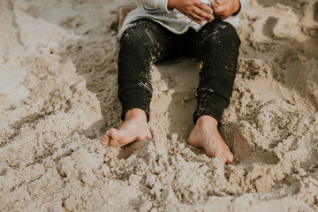 Detail of girls legs with dirty feet from sand siting and digging in sand during the sunny summer...